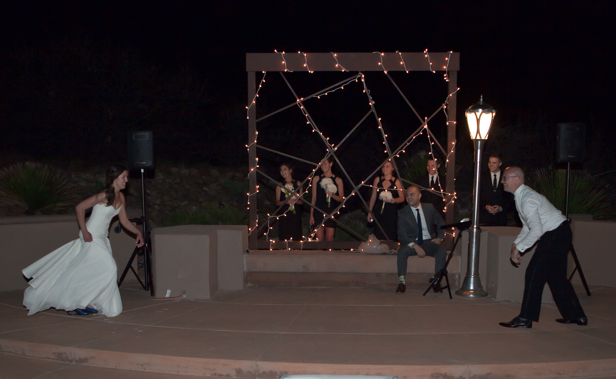 First dance — wide shot showing full ceremony stage, wedding party watching from behind, custom lamppost, and bridesmaids in black MaxMara dresses